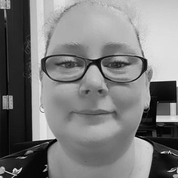 Black-and-white photo of Carine Huscroft, smiling, wearing dark-rimmed glasses.